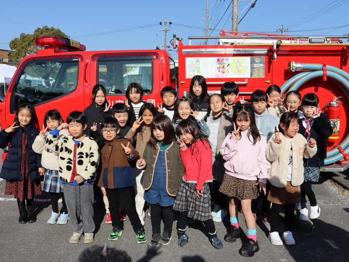 自分たちの絵がラッピングされた、消防団第1分団車両の前で集合写真を撮る犬山北小学校の児童