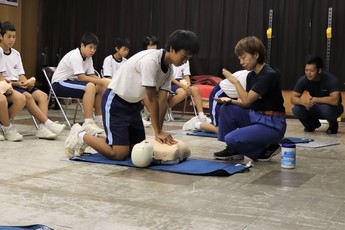 先生役の女性消防団員の前の人形に胸骨圧迫を行う男子中学生