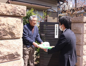 個人宅の前で市役所男性職員から書類を受け取る町会長の男性