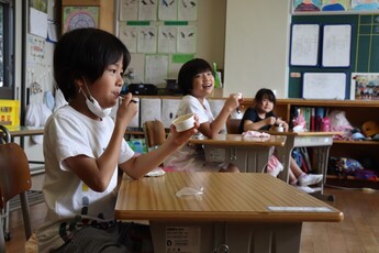 教室でジェラートのカップを手に食べている児童3人