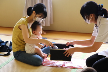 講師の女性に使用したパンダのおもちゃを渡す赤ちゃんをひざにのせた女性