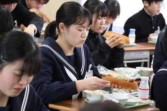 手前にパンにウインナーをはさむ女子生徒、奥にドッグを口へ運ぶ女子生徒