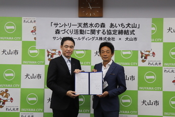 協定書を手にする藤原常務執行役員（左）と原市長（右）の写真